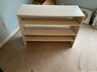 Two white stacking shoe organizers placed on carpet floor, showing open shelf design and rectangular shape.
