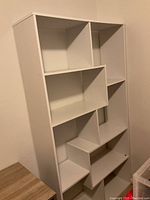 White bookshelf with multiple open shelves in various geometric shapes, photographed at an angle showing depth and condition.