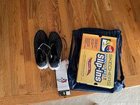 View of black Under Armour Flow Velociti Wind sneakers alongside Broncos socks and Skechers shoe box on wooden floor, showing sneaker style and sock design.