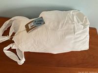 Photo of white sheet set labeled X-Long Twin with packaging showing tied straps and label