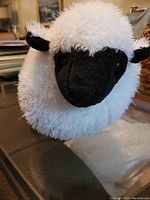 White fluffy sheep plush with black face and ears on a glass table.