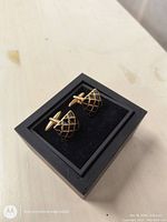 Photo of two men's cufflinks with gold-tone lattice pattern on black, displayed in black box with felt lining.