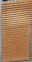 Front view of a single faux wood blind with 2-inch wide slats in a light brown pine finish, suitable for window covering.