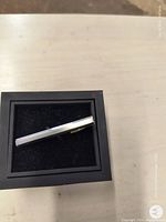 Silver tie clip displayed on a black cushioned holder showing polished shiny surface and slim design.