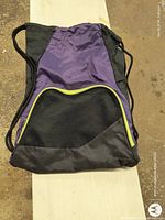 Photo of a purple and black convertible tote bag with drawstring straps and front mesh zippered pocket on a light surface.
