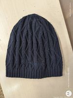 Dark knit winter beanie toque laid flat on a light surface, showing cable knit and ribbed brim