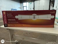 Box of Vanity Fixture from the Portfolio Raylo Collection, indicating chrome finish with a mirrored backplate and ribbed frosted glass shade.