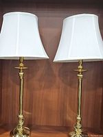 Pair of brass table lamps with white fabric trapezoid-shaped shades placed on wooden surface