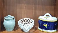 Photo shows all three items: blue ceramic lidded jar, white ceramic woven basket, and blue Italian lidded jar with floral motif in a wooden shelf.
