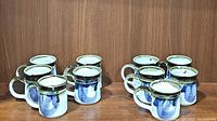 Ten ceramic mugs on a wooden surface, showing full set and arrangement.