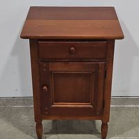 Front view of solid wood chairside cabinet showing drawer and closed door.