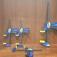 Four Irwin Quick-Grip bar clamps arranged on brown wood surface and wood background. Three clamps upright, one clamp horizontally laid.