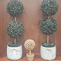 Front view of two double sphere green foliage artificial topiary trees in white pots and smaller wooden sphere tree sculpture centered between them.