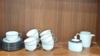 Set of 12 white cups stacked on 10 saucers with creamer and sugar container beside them, showing full lot contents.