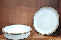 Two Heath ceramic dishes on wooden shelf, one deep dish and one platter with white glaze and natural clay rim.