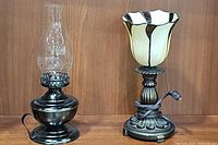 Metal vintage oil lamp with etched glass chimney and flower-shaped Tiffany style lamp on wooden shelf.