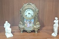 View of mantle clock flanked by two sculpture figurines on wooden surface.