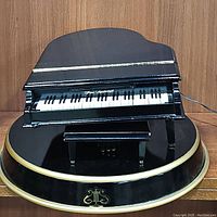 Front view of the Mr. Christmas black grand piano music box on its round base with gold trim and emblem.