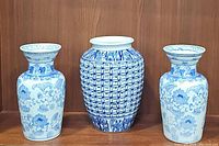 Frontal view of the three porcelain vases arranged side by side on a wooden surface, showing overall design and relative sizes.