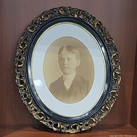 Oval framed sepia-toned photograph of young boy with detailed black and gold carved frame