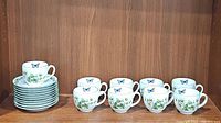 Set of 9 porcelain teacups and 9 matching saucers arranged on shelf, showing overall quantity and pattern