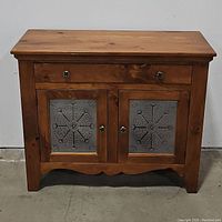 Front view of closed pie safe showing single drawer, two cabinet doors with decorative punched tin panels and green floral knobs