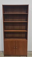 Front view of the teak wooden bookcase showing 4 shelves and 2-door cabinet below.