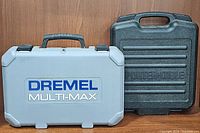 Closed Dremel Multi-Max gray carrying case and closed black Porter-Cable case side by side against wooden background.