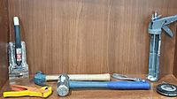 Various hand tools including a hammer, mallet, pipe cutter, and caulking gun arranged on a wooden surface