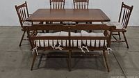 Full view of wooden trestle table with four chairs and bench, cushions tied to each seat.