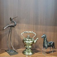 Photo of the entire lot showing the brass tea kettle with stand in the center, metal bird sculpture on the left, and metal horse sculpture on the right.