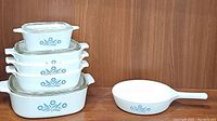 Set of 5 rectangular CorningWare casserole dishes with lids, nested stacked by size and one round handled pan, all with blue cornflower design.