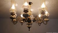 Overall view of the full antique brass chandelier showing six light bulbs with frosted glass hurricane shades and floral hand-painted porcelain bases.