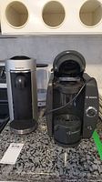 Two coffee makers side by side on a counter, Nespresso silver and black on left, Bosch Tassimo black on right
