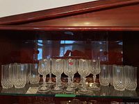 Shelf showing stemmed crystal wine glasses with cut designs and faceted bases, flanked by faceted tumblers.