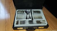 Overview of cutlery set inside an open black suitcase showing forks, spoons, knives.