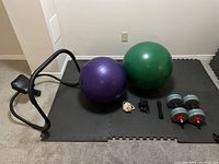 Full view of exercise balls, dumbbells, hand grips, ab roller, and foam mats on floor.