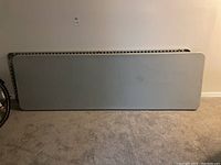 Two gray folding tables nested and leaning against a wall, folded flat.