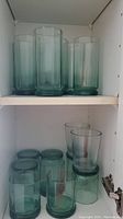 Shelves with green glasses of various sizes and shapes, showing 12 total glasses with cylindrical forms and green tint.