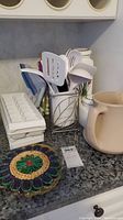 Countertop with white spatulas in metal container, ice cube tray, ceramic container, and woven pot holder