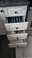 Four kitchen drawers open showing kitchen cutlery, flatware, and utensils inside