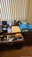 Full overview of desk and drawer filled with various office supplies including paper reams, pens, and small desk items