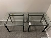 Pair of glass top side tables with black metal legs viewed from above and side angles showing design and condition.