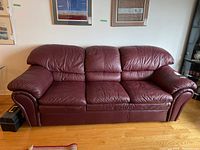 Full frontal view of burgundy leather three-seat sofa on hardwood floor beneath framed artwork