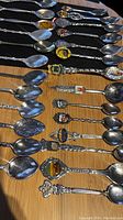 Top view of 19 souvenir spoons laid on black felt showing colorful enamel crests and twisted ornate handles