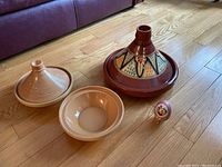 Full lot including both large and small tagines, ceramic bowl, and decorative ornament arranged on wood floor