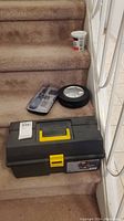 Photo of toolbox, tool set case, and Subaru tire-shaped item displayed on carpeted stairs.