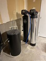 Wide view showing two tall filter tanks and a round brine tank on concrete floor