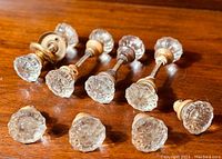Full view of eight antique glass doorknobs laid on wood surface, four assembled sets and four single side knobs.