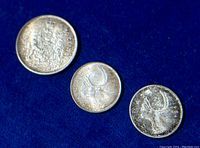 Three circulated Canadian coins on blue fabric: 1964 quarter, 1965 half dollar, 1966 quarter. Coins display caribou heads on quarters and Coat of Arms on half dollar.